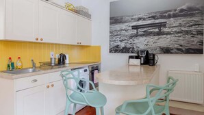Une cuisine avec des meubles blancs, un pare-feu jaune et une machine à café.