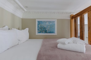A hotel room with a bed, pillows, a painting, and a wooden beam structure.