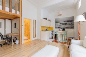 Un appartement moderne doté d’un plancher en bois, d’un coin repas, d’une cuisine avec un crédence jaune et d’un grand tableau en noir et blanc.