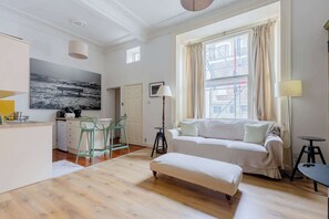 A modern living room with a sofa, ottoman, and a dining area with chairs and a table.