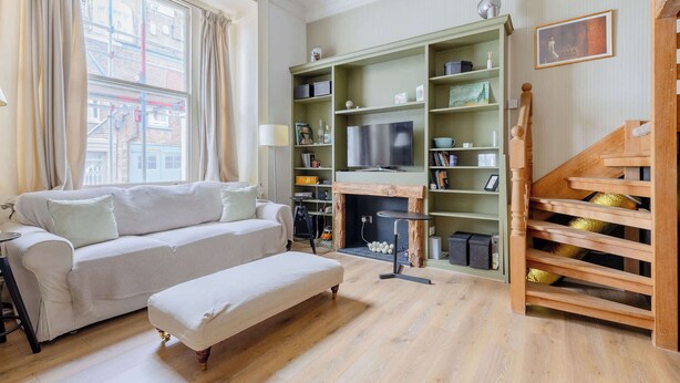 Un salon comprenant un canapé, un banc, une cheminée, un téléviseur et un escalier avec une rampe en bois.