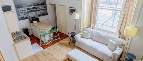 A compact living space with a kitchenette, a sofa, a dining area, and a large window with curtains.