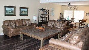 A living room with two brown leather sofas, a wooden coffee table, and a dining area with a table and chairs. - Pelican Point #6 -Great Complex! Great Views! Cool off in the swimming Pool! (Port Mansfield)