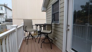 A balcony with a table and two chairs, a sliding glass door, and a white railing.