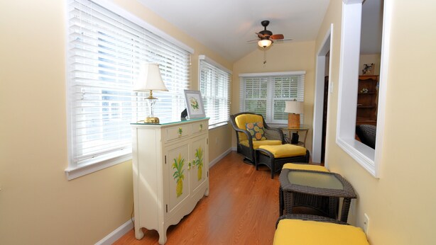 A hallway with a white cabinet, two wicker chairs, a small table, and a ceiling fan.