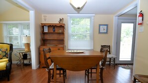 A dining area with a wooden table and chairs, a bookshelf, and a window with blinds.