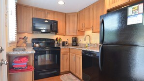 A compact kitchen with wooden cabinets, a black refrigerator, a microwave, a stove, and a dishwasher.