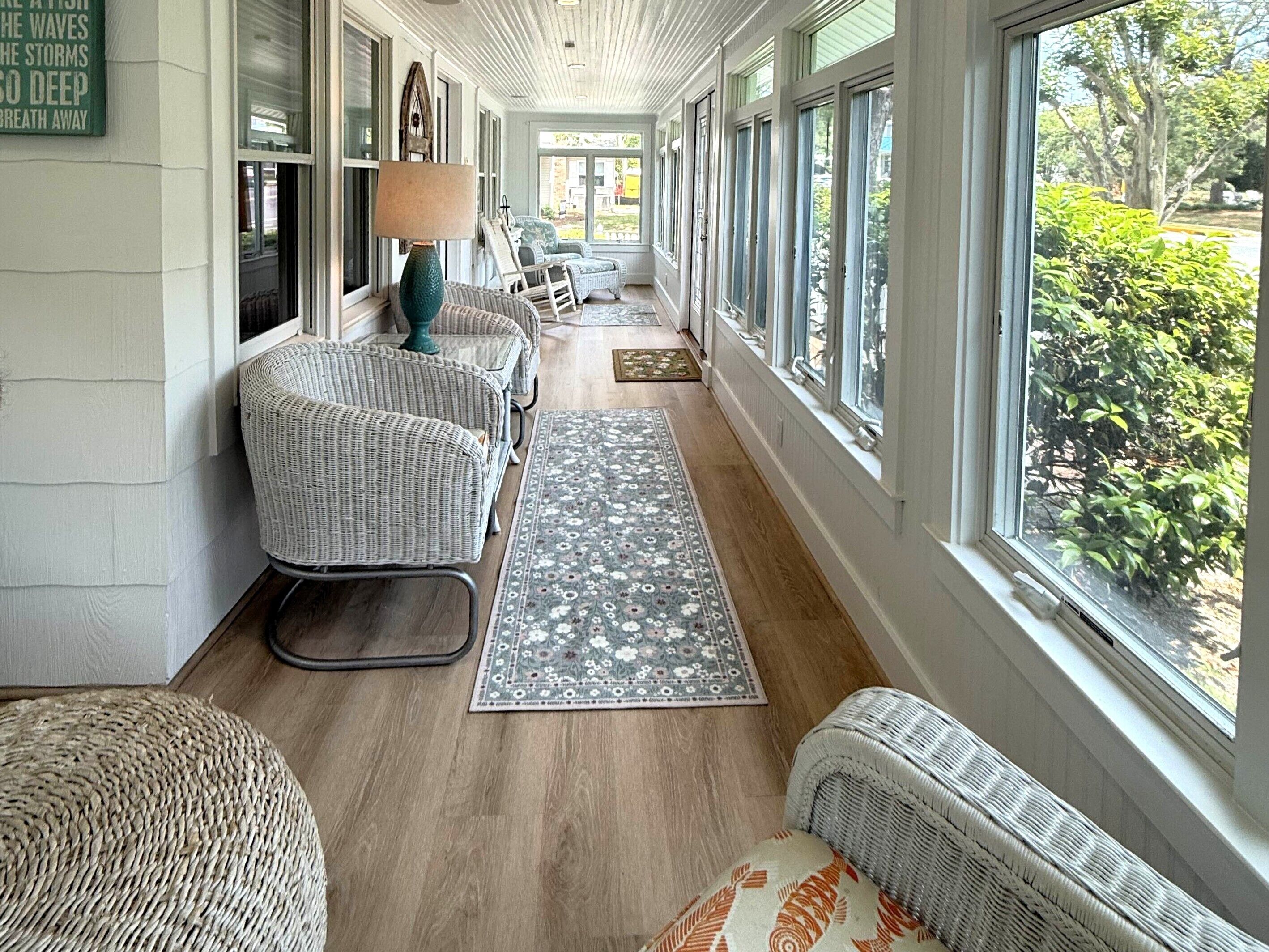 A covered porch with wicker furniture, a lamp, and a view of greenery.
