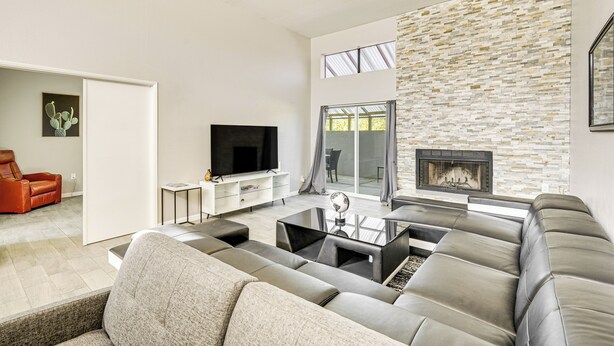 Un salon moderne avec un canapé d’angle, un téléviseur à écran plat, une cheminée et un mur décoratif en pierre.