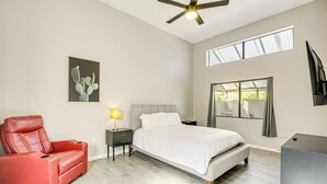 Une chambre à coucher avec un lit, un fauteuil rouge inclinable, une table de chevet avec une lampe, un ventilateur de plafond et une fenêtre avec des rideaux.
