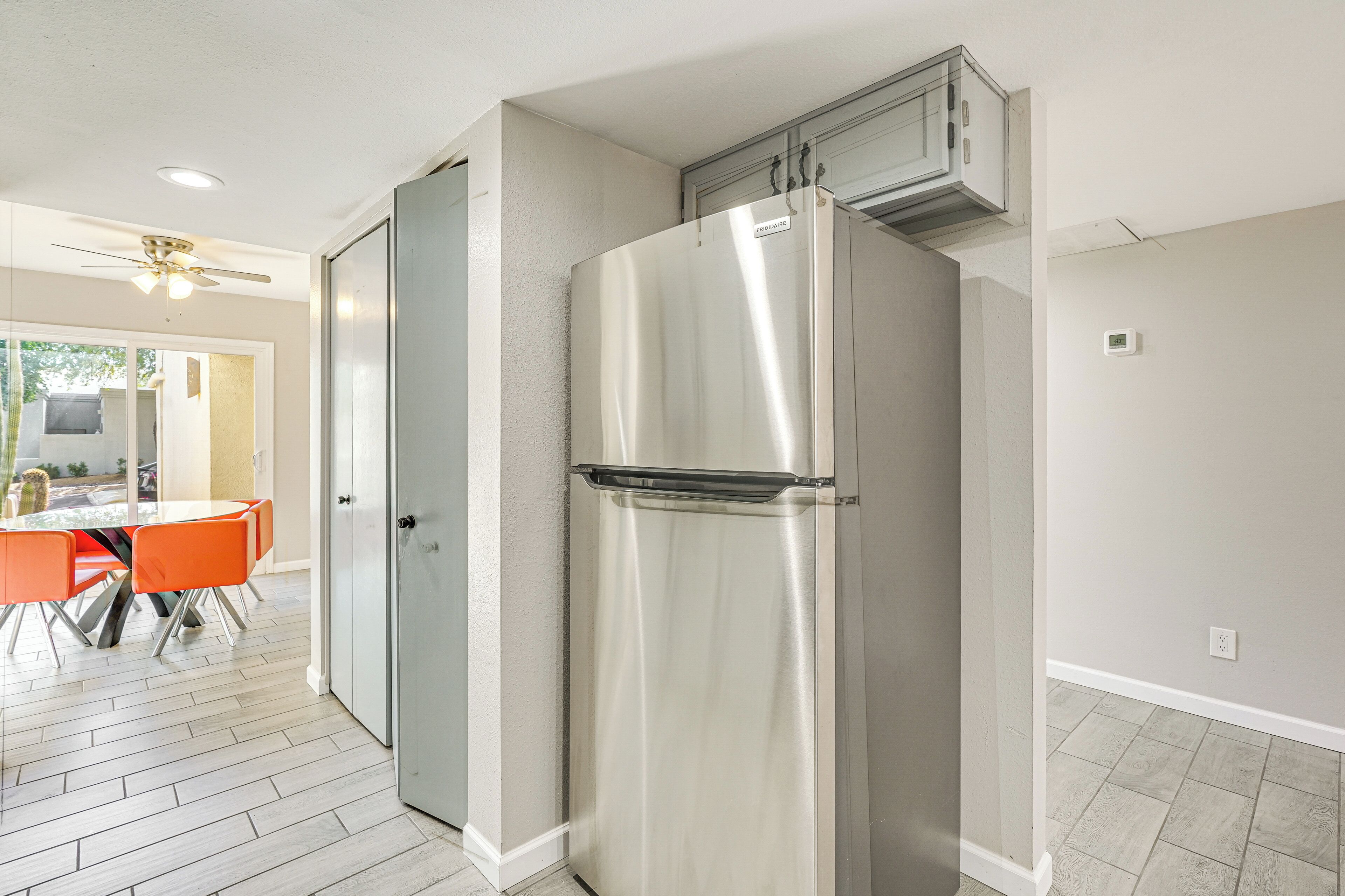 A kitchen with a stainless steel refrigerator, a dining table with orange chairs, and a ceiling fan.