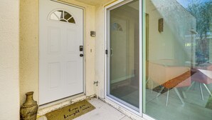 Une porte blanche avec une petite fenêtre, une porte-fenêtre coulissante et un paillasson portant un message.