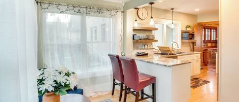 A kitchen with a central island, wooden chairs, a dining table, and a vase with flowers.