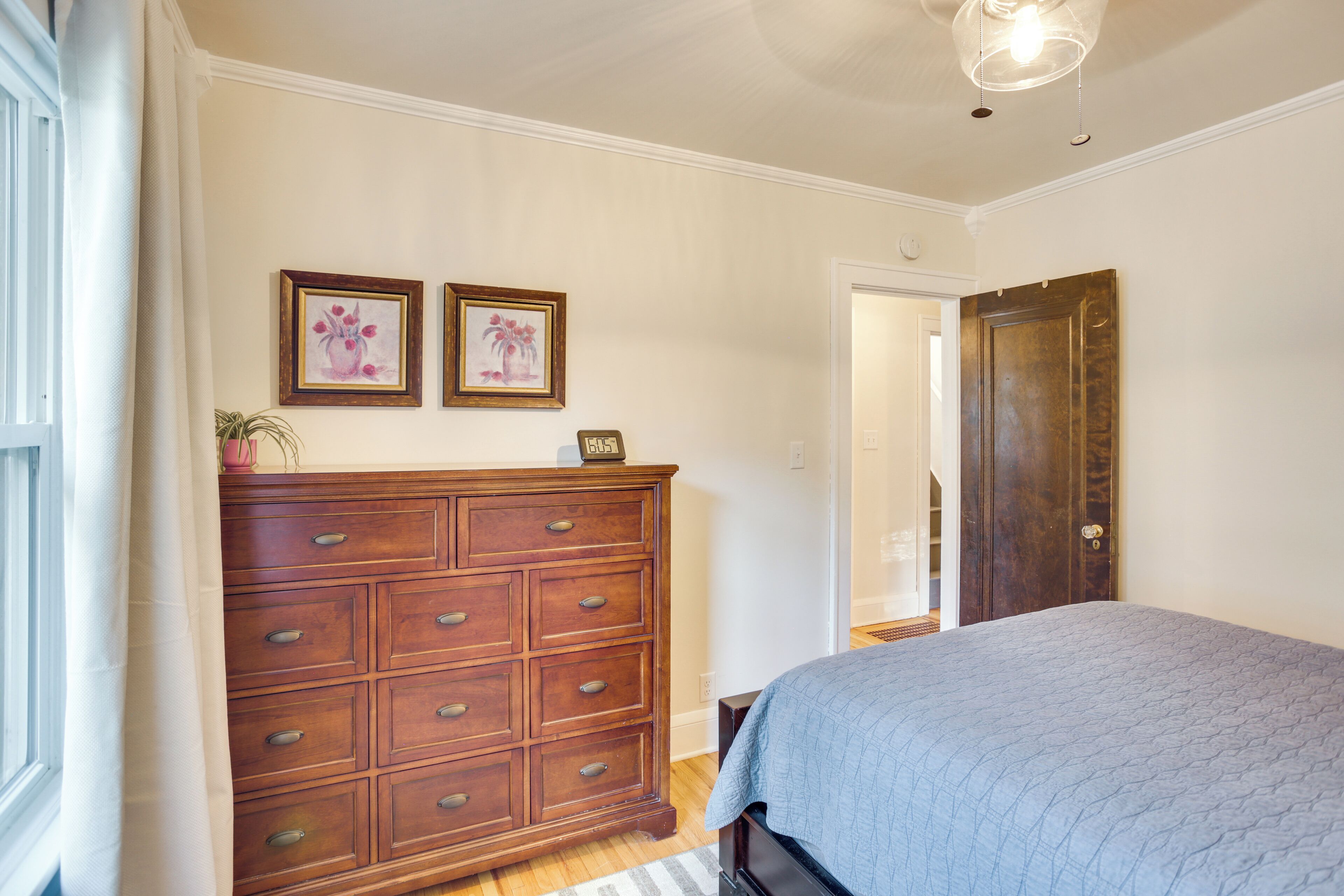 A bedroom with a large bed, wooden dresser, and two framed pictures on the wall.