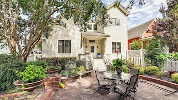 A two-story house with a patio area featuring a table and chairs, surrounded by potted plants and a brick border.