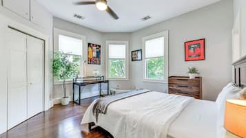 A bedroom with a bed, a desk, a chair, a dresser, and a ceiling fan.