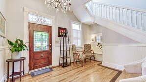 Ein geräumiger Eingangsbereich mit Holzdielenboden, einer Holztür mit Buntglas, einem Chandelier und einer Treppe mit weißen Geländern.