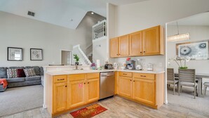 A modern kitchen with wooden cabinets, a dishwasher, and a dining area with a table and chairs. - 15 Mi to Universal: Home w/ Pool (Kissimmee)