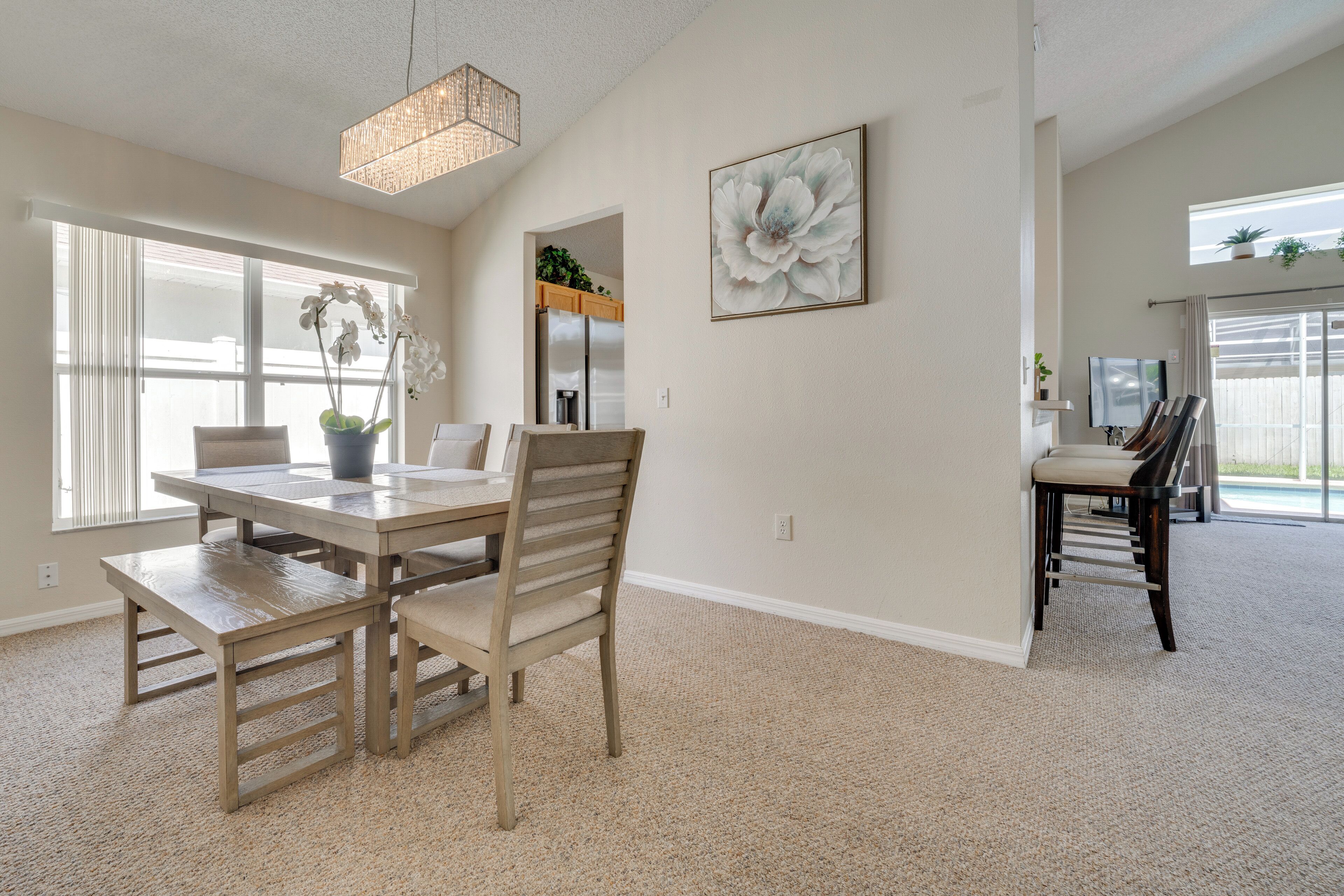 A spacious dining area with a wooden table and chairs, a chandelier, and a large floral painting on the wall.