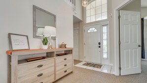 A hallway with a wooden console table, a mirror, and a framed quote. There are white doors and a carpeted floor. - 15 Mi to Universal: Home w/ Pool (Kissimmee)