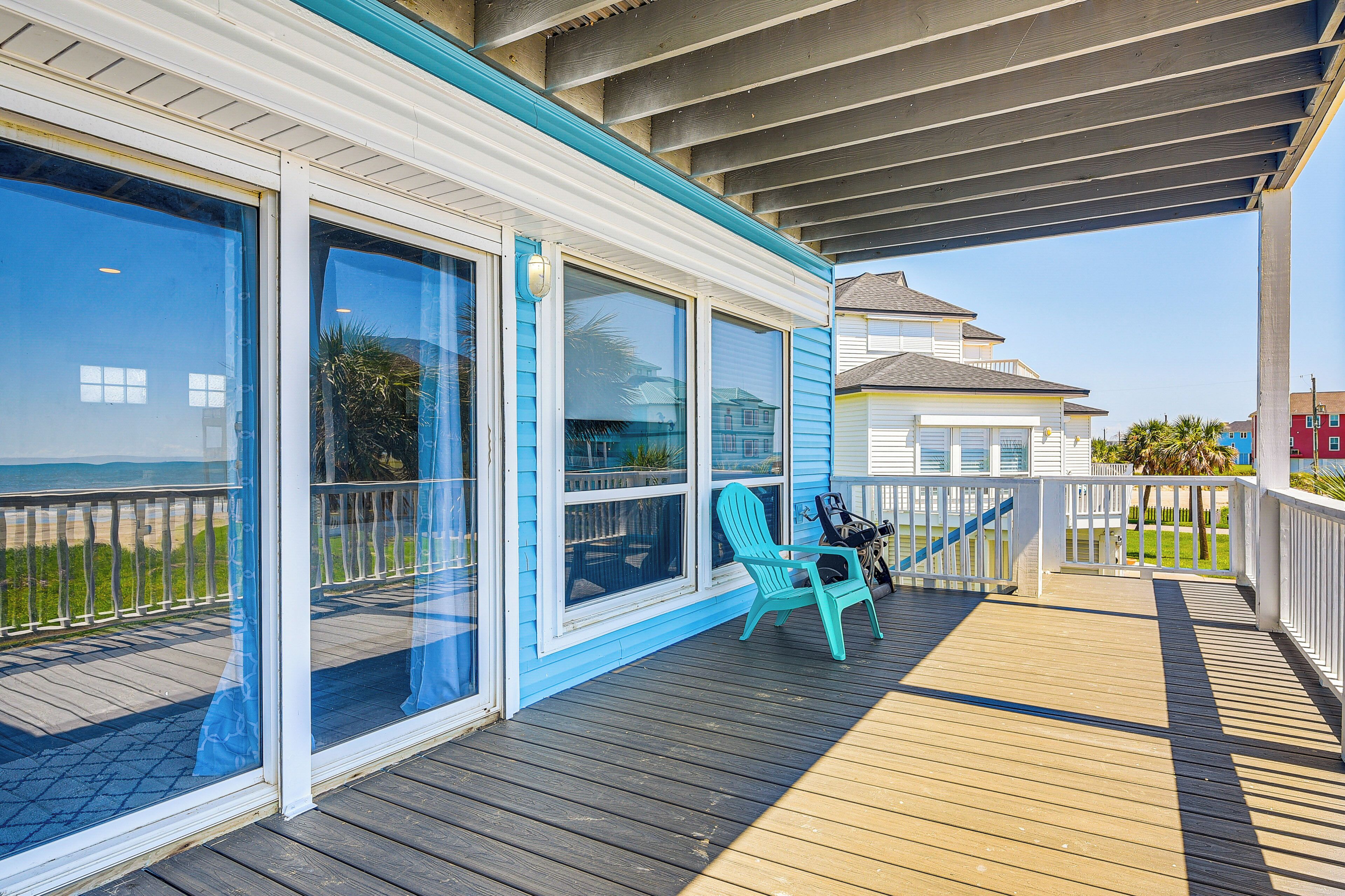 Une terrasse couverte avec vue sur la plage, une chaise Adirondack turquoise et une petite table.
