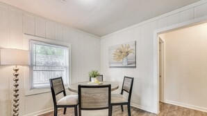 Un coin repas avec une table ronde, quatre chaises, un lampadaire, une fenêtre avec des stores et un tableau au mur.