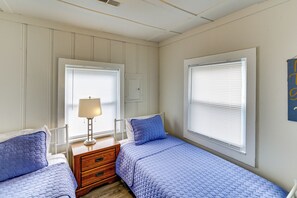 A bedroom with two beds, a nightstand, a lamp, and a window with blinds.