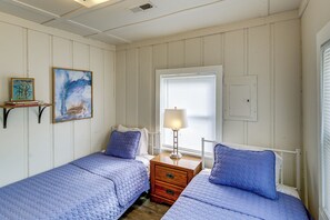 Een kamer met twee bedden, een nachtkastje met lamp, een raam met jaloezieën en een schilderij aan de muur.