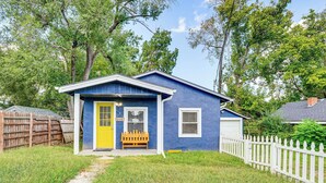 Une petite maison de plain-pied, avec une façade bleue et une porte d’entrée jaune.