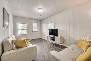 Una habitación con un sofá de cuero blanco, un televisor sobre un mueble bajo y una puerta con ventanal.