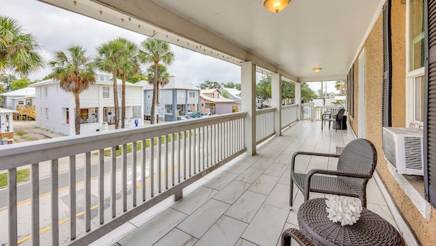 Een overdekt balkon met een witte railing, rieten meubilair en uitzicht op de straat en gebouwen.