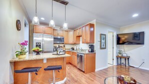A modern kitchen with wooden cabinets, stainless steel appliances, and a bar area with stools. - Walk to Nights of Lights: Dtwn St Augustine Stay (St. Augustine)