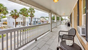 A covered balcony with a white railing, wicker furniture, and a view of the street and buildings. - Walk to Nights of Lights: Dtwn St Augustine Stay (St. Augustine)