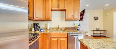 A kitchen with wooden cabinets, a stainless steel dishwasher, granite countertops, and a built-in oven.