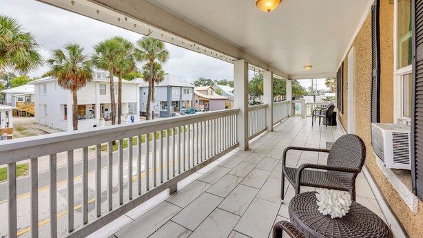 A covered balcony with a railing, wicker furniture, and a view of the street and buildings. - Walk to Nights of Lights: Historic Downtown Stay (St. Augustine)