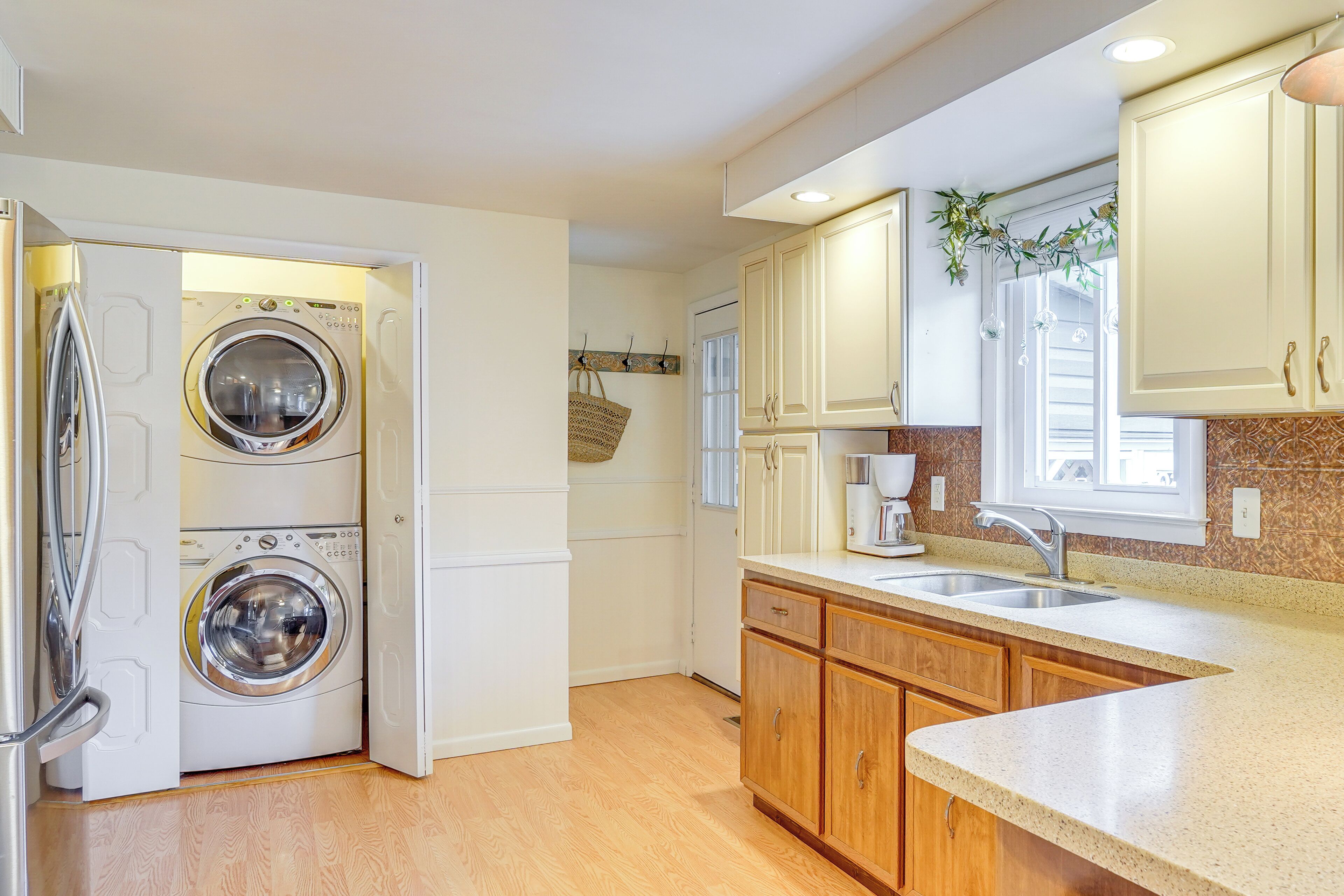 Une cuisine compacte dotée d’un lave-linge et d’un sèche-linge intégrés, de meubles en bois, d’un évier et d’une fenêtre offrant une belle vue.