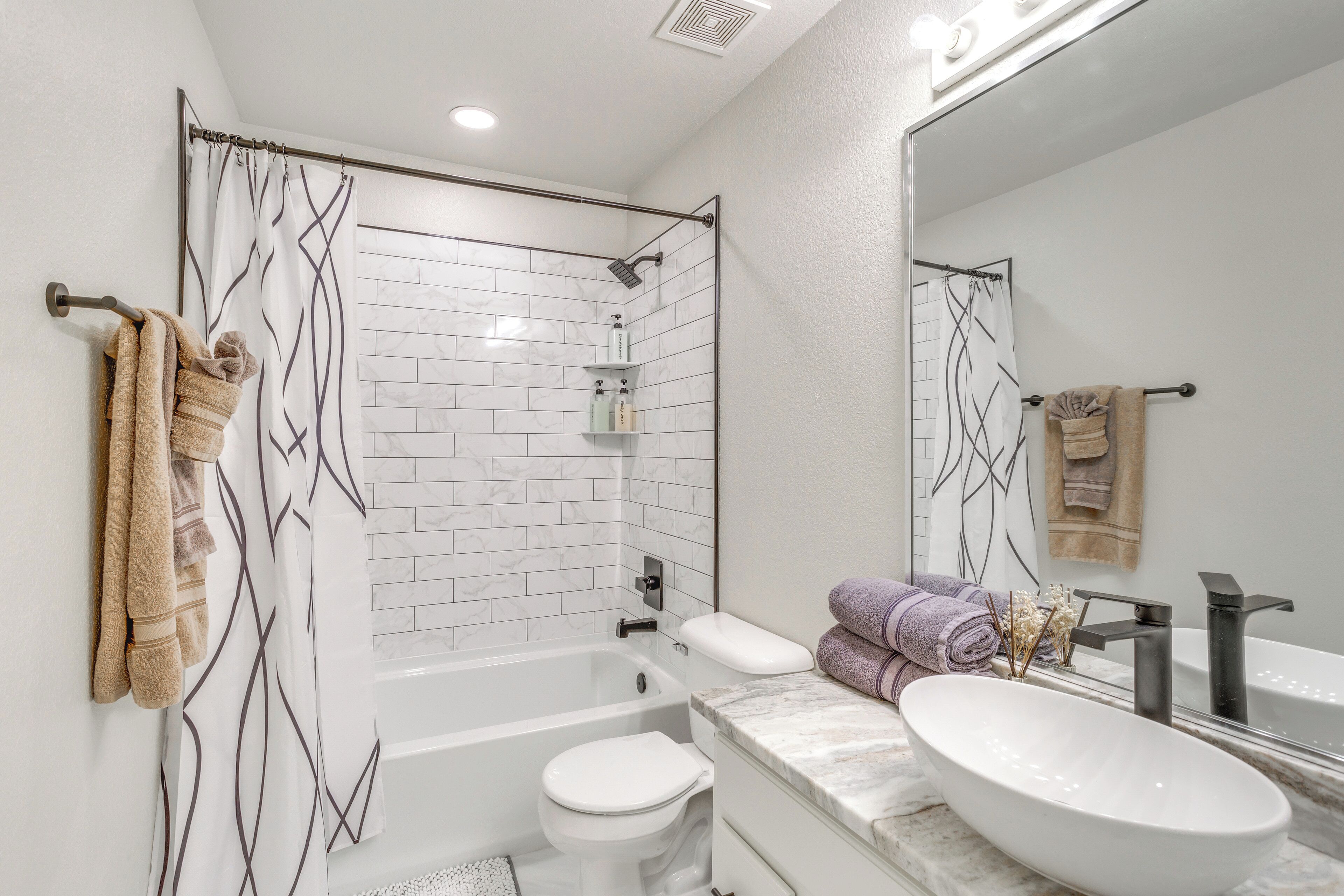 A modern bathroom with a bathtub, toilet, and vanity with a large mirror.