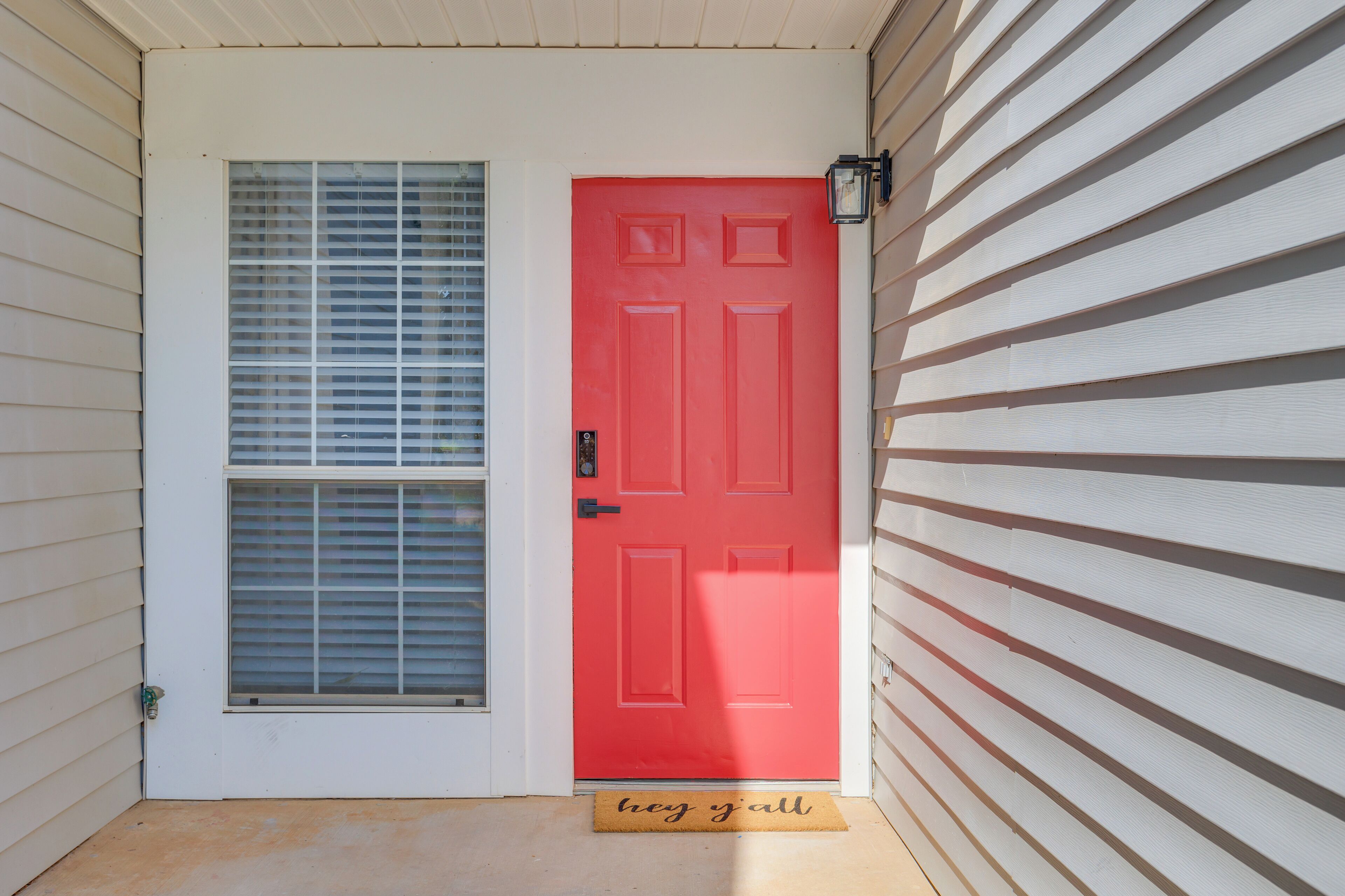 A red door with a window above it, a doormat with "neg yall" text, and a white exterior wall.
