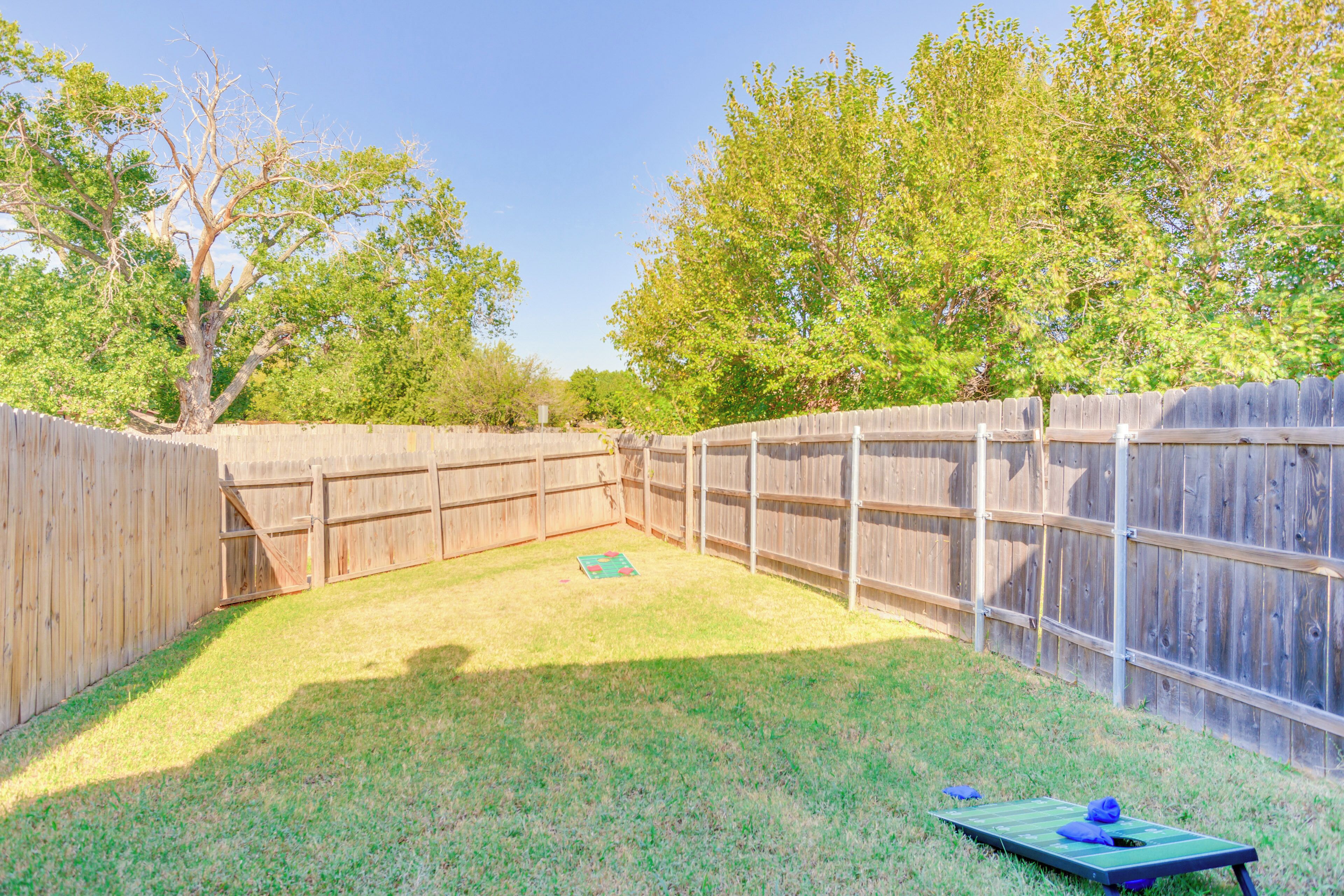 A fenced backyard with a grassy area, a wooden deck, and trees in the background.