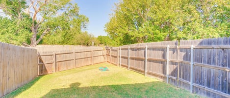 A fenced backyard with a grassy area, a wooden deck, and trees in the background.
