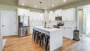 A modern kitchen with white cabinets, stainless steel appliances, and a central island with bar stools. - 1 Mi to Pools: Chic Lava Hot Springs Home (Lava Hot Springs)