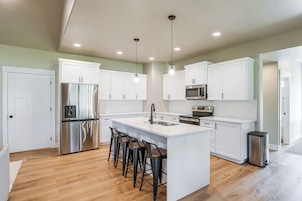 Una cocina moderna con armarios blancos, electrodomésticos de acero inoxidable y una isla central con taburetes de bar.