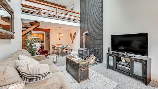 A loft-style living room with a high ceiling, a fireplace, a television, and a cozy seating area. - Bartlett Condo: 1 Mi to Attitash Mountain Resort! (Bartlett)