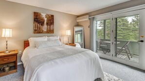 A bedroom with a large bed, two bedside lamps, a painting on the wall, and a sliding glass door leading to an outdoor deck. - Bartlett Condo: 1 Mi to Attitash Mountain Resort! (Bartlett)