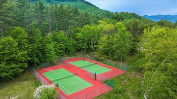 Cancha de tenis al aire libre rodeada de un bosque denso y montañas.
