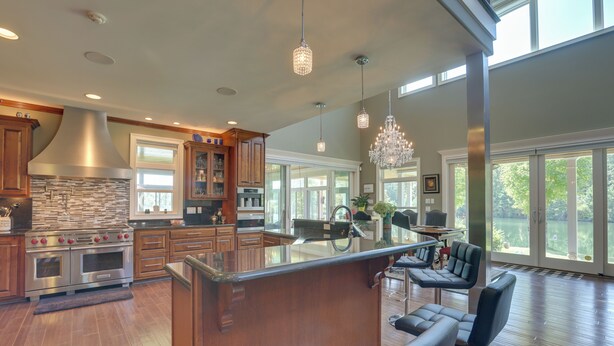 A spacious kitchen with a large island, stainless steel appliances, and a view of a lake through large windows. - Fish, Swim & More: Lakefront Alabaster Home (Alabaster)