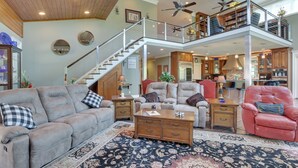 A spacious living area with a high ceiling, a staircase leading to an upper level, and a kitchen area visible in the background. - Fish, Swim & More: Lakefront Alabaster Home (Alabaster)