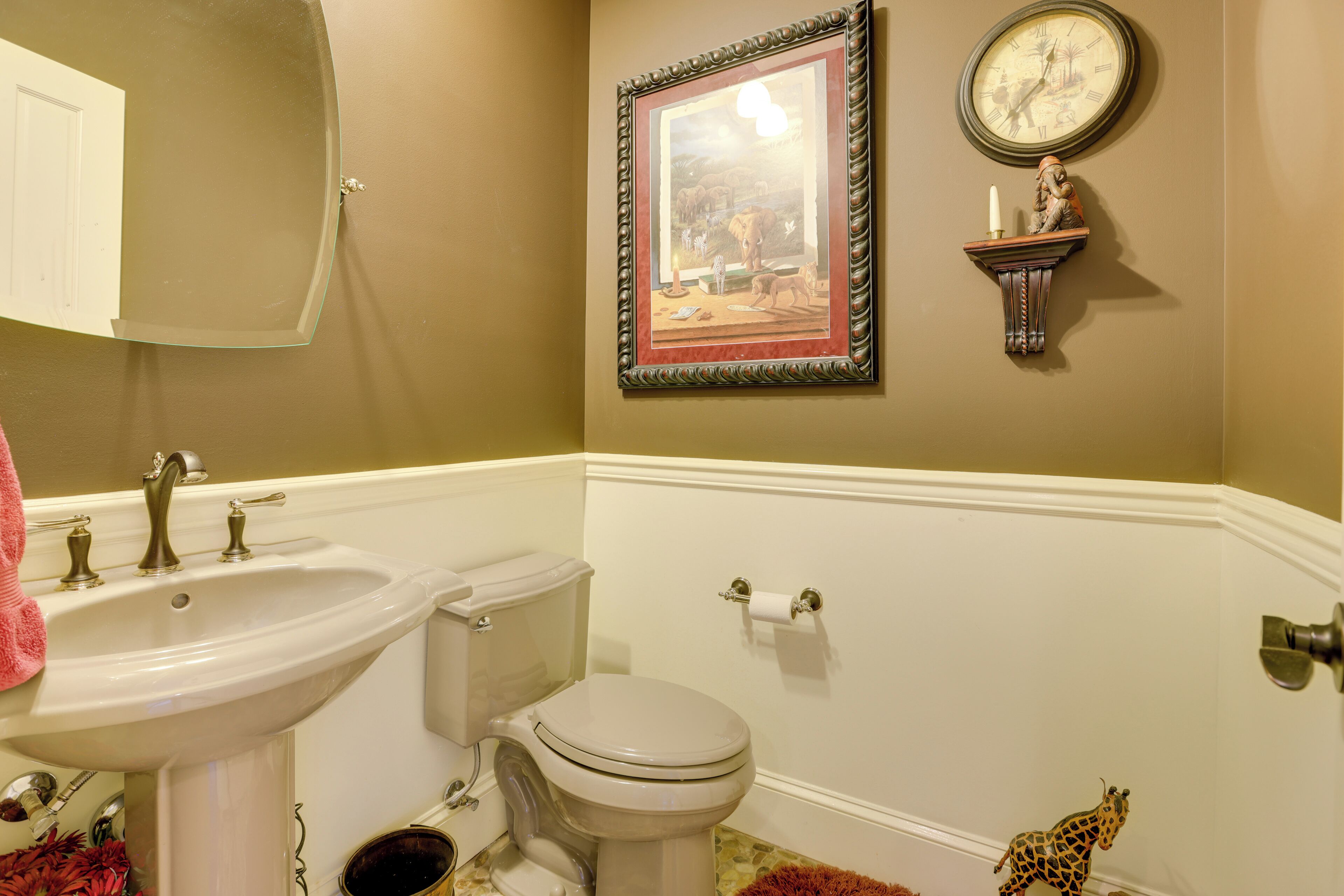 Une salle de bain avec un lavabo, des toilettes, un tableau encadré et une horloge au mur.