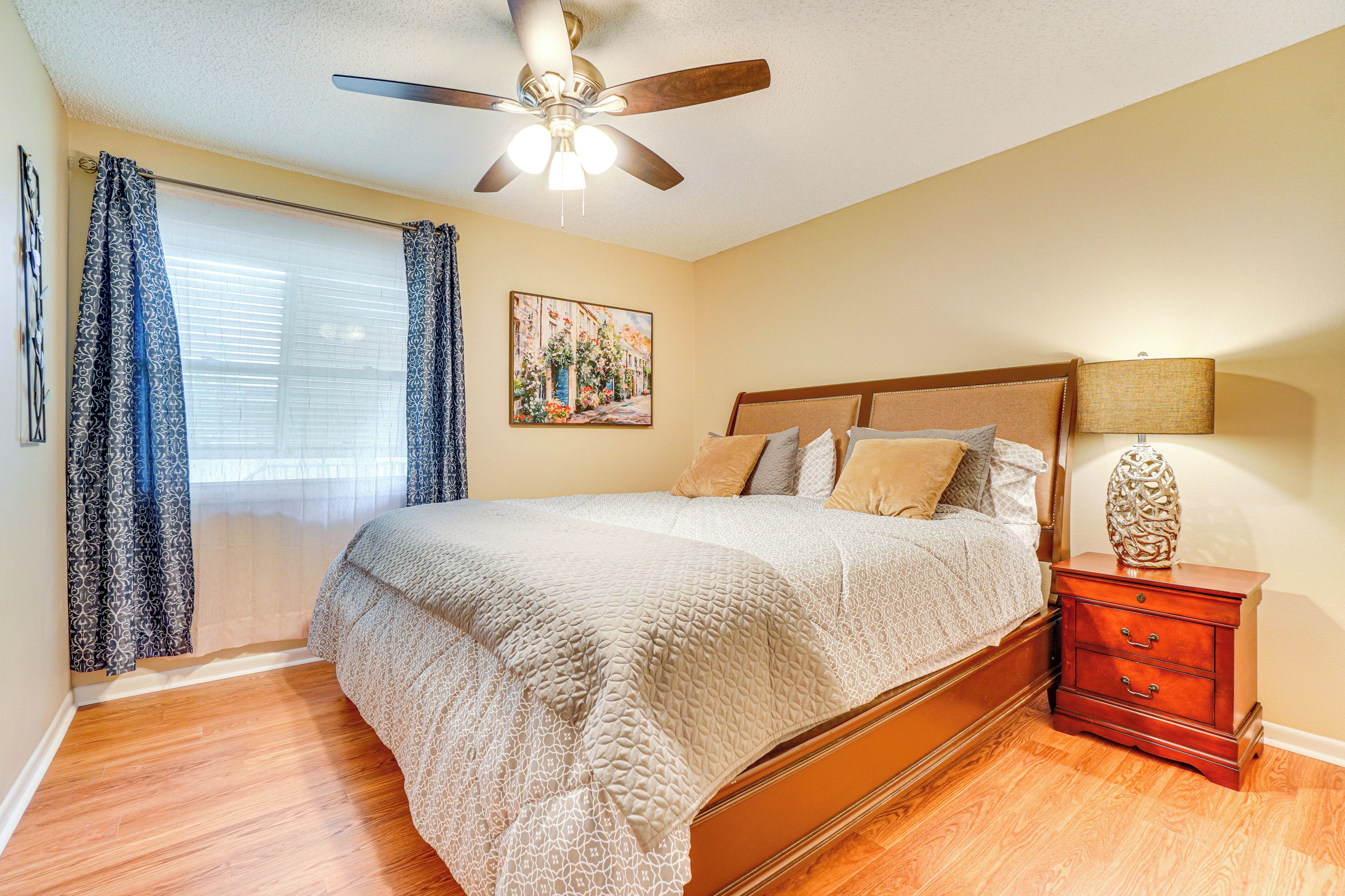 A bedroom with a bed, a nightstand, a ceiling fan, and a window with curtains.