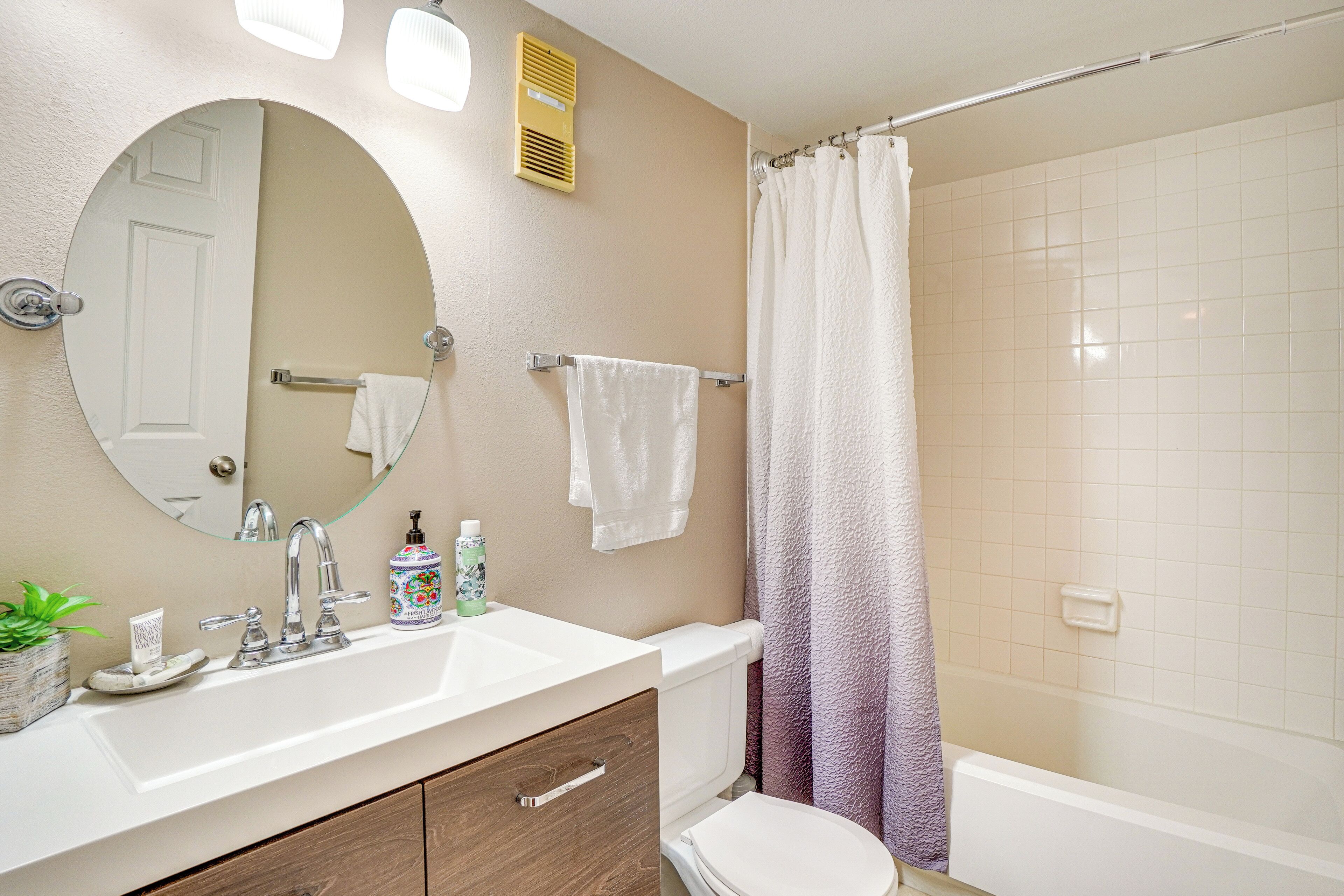 Un baño con un lavabo blanco, espejo, inodoro, cortina de ducha y un perchero.
